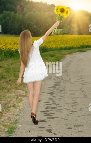 Jeune femme en robe courte blanche avec des tournesols à country road Banque D'Images