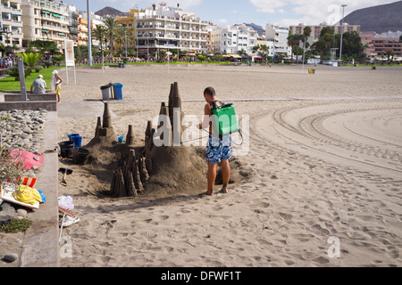 Sculpteur de sable de l'eau d'un sac à dos, des pulvérisations sur le château de sable de la préserver, plage de Los Cristianos, Tenerife, Îles Canaries Banque D'Images