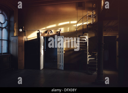 La lumière du soleil filtrée dans une grande salle vide avec escalier à vis et ouvrir les portes doubles Banque D'Images