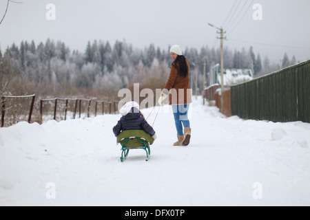 Jeune mère roule son petit mignon filles sur un traîneau en hiver jour Banque D'Images