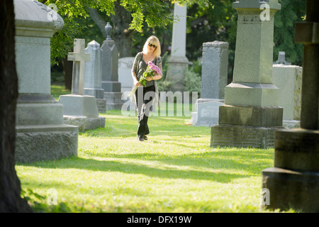 Une femme marche à travers le cimetière avec des fleurs Banque D'Images
