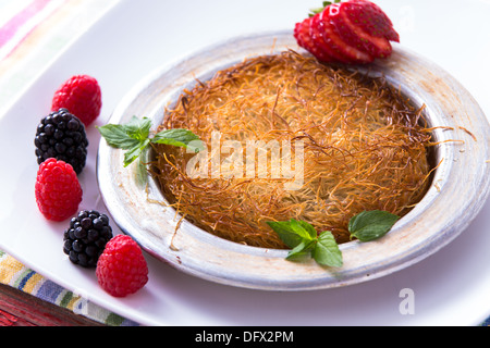 Kunefe dessert turc servi dans la plaque d'aluminium sur une plaque blanche avec la menthe et fraise en tranches le long rouge et noir Banque D'Images