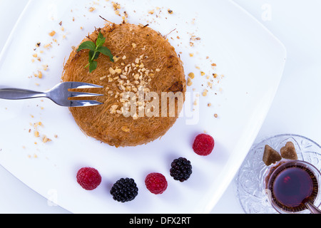 Kunefe dessert turc servi sur une plaque blanche avec des feuilles de menthe, de baies rouges et noires avec du thé chaud turc Banque D'Images