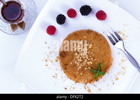 Kunefe dessert turc servi sur une plaque blanche avec des feuilles de menthe et de tranches de fraise le long de baies rouges et noires Banque D'Images