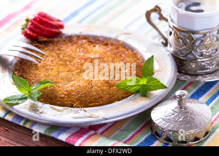 Kunefe dessert turc servi dans la plaque en aluminium sur une table de pique-nique avec la menthe et fraise en tranches avec Bain turc Banque D'Images