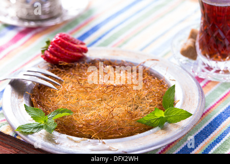 Kunefe dessert turc servi dans la plaque en aluminium sur une table de pique-nique avec la menthe et fraise en tranches avec Bain turc Banque D'Images