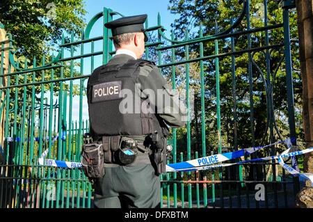 Un policier de la garde PSNI la porte d'un parc qui a une bande de police à travers elle à la suite d'un crime Banque D'Images