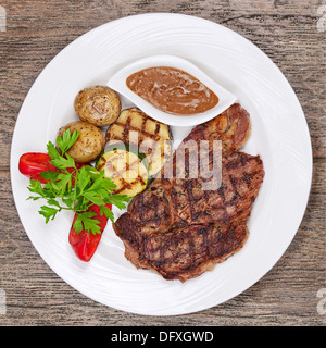Les steaks grillés, pommes de terre au four et légumes sur plaque blanche sur fond de bois. Banque D'Images