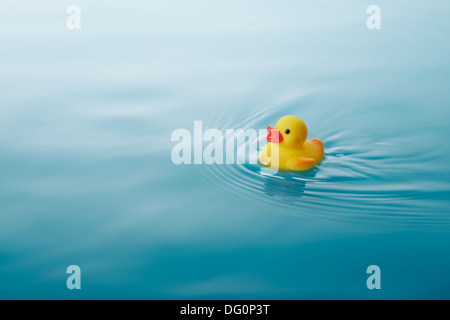 Canard en caoutchouc jaune natation sur l'eau provoquant des vagues et ondulations Banque D'Images