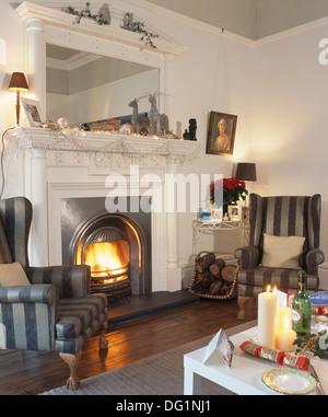 Rayé gris fauteuils de chaque côté d'une cheminée au-dessous d'un grand miroir dans la salle de séjour maison décorée pour Noël Banque D'Images