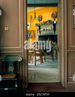 Hall lambrissé peint en gris avec des meubles incrustés chaise à côté de porte ouverte sur salle à manger pays jaune Banque D'Images