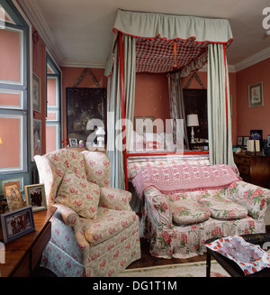 Canapé et fauteuil à motifs floraux en rouge traditionnelle chambre avec lit à baldaquin avec des rideaux vert pastel Banque D'Images