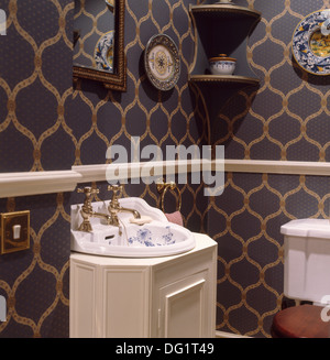 Les robinets en laiton sur bleu et blanc bassin floral en blanc coiffeuse dans un vestiaire au dos gris et or papier peint à motifs Banque D'Images