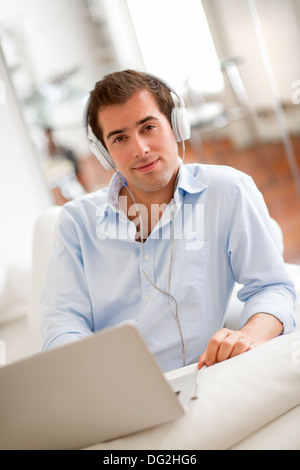 L'homme à l'écoute de la musique avec des écouteurs sur un ordinateur portable, sitting on sofa Banque D'Images