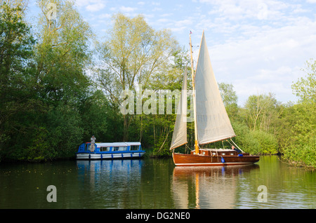 Yacht de voile sur la rivière Bure, Norfolk Broads, en Angleterre, au cours de la lancer péniche amarrée sous les arbres. Banque D'Images