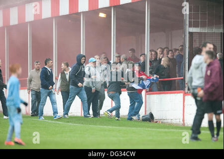 Atherstone, Warwickshire, Royaume-Uni. 12 octobre, 2013. Un groupe de fans à partir de l'extrémité de la route sol Sheepy marcher autour du périmètre de la hauteur et de l'échelle les clôtures pour attaquer le supporters visiteurs (Barrow AFC). Un feu d'artifice a également été lancée en direction de la terrasse de la voiture qui suit. Un drapeau a été volé de la Barrow AFC fans et ensuite mis le feu à l'aide d'un artifice allumé. Atherstone Président Rob Weale a présenté ses excuses pour ce qui s'est produit et a juré de poursuivre les auteurs. Banque D'Images