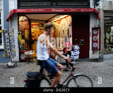 Un cycliste passant d'une boutique de dentelle à Bruges Belgique Banque D'Images