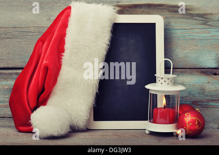 Décoration de Noël avec une bougie dans une lanterne et de pans de blackboard with Santa's hat sur fond de bois Banque D'Images