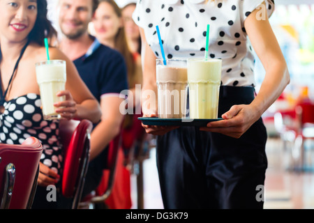 Des amis ou des couples eating fast food et de boire des milk-shakes sur bar en restauration rapide américaine diner, la serveuse est prise des commandes Banque D'Images