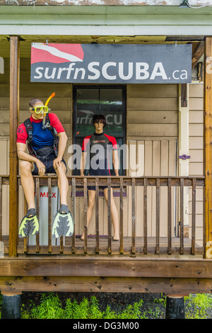 Les mannequins vêtus de combinaisons assise sur une balustrade avec un tuba et des lunettes portant en face d'un magasin de sport de l'eau. Banque D'Images