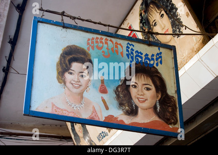 Enseignes peintes montrant les femmes et écrit en Khmer accrocher au-dessus d'un salon de beauté sur une rue de ville de Phnom Penh, Cambodge. Banque D'Images