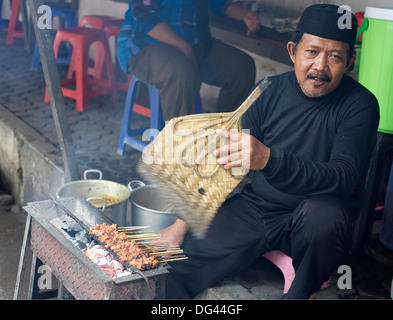 Musulman dans le marché de la cuisson du poulet satay, attisant les braises avec un ventilateur de feuille de palmier, Solo, Java, Indonésie, Asie du sud-est Banque D'Images