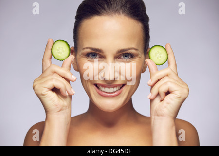 Portrait of young Beautiful woman holding tranches de concombre dans les mains près de son visage sur fond gris. Banque D'Images