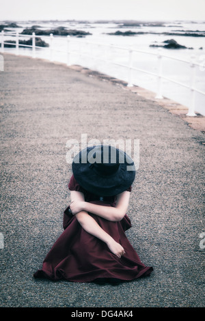 Une femme dans une robe rouge avec un chapeau noir est assis sur un quai Banque D'Images