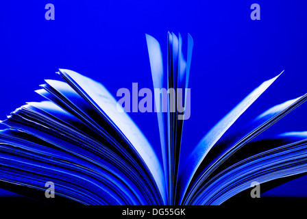 Un grand livre unique assis avec des pages ouvertes sur un bureau et le fond bleu Banque D'Images