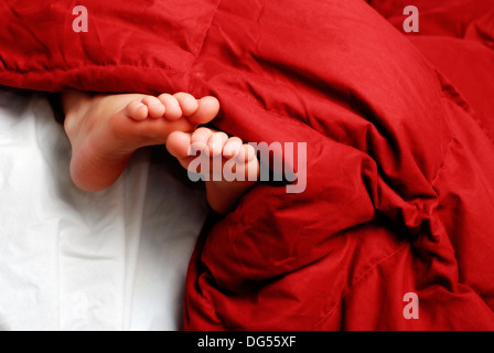 Petite fille dormir avec pieds poussant hors de couvertures Banque D'Images