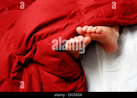 Petite fille dormir avec pieds poussant hors de couvertures Banque D'Images