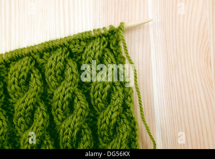 Câble corde enroulée vert knitting stitch sur l'aiguille, sur un fond de bois Banque D'Images