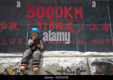 Kid tibétaine en face d'une signalisation routière.Les signes qui disent nous sommes exactement 5000 km de Shanghai, sur la route de l'amitié au Tibet Banque D'Images