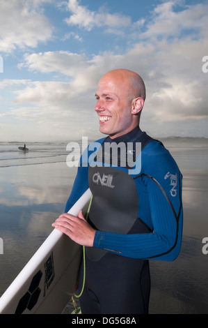 Homme chauve smiling holding surf board sur plage avec coucher de soleil Banque D'Images