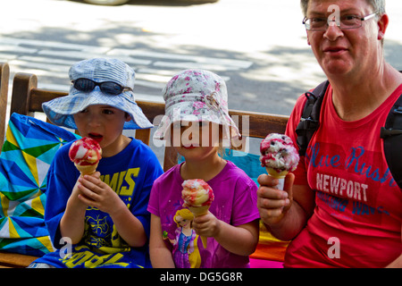 Homme d'âge moyen de traiter ses filles à la glace tout en étant assis sur un banc sur le trottoir à Sausalito, Californie. Banque D'Images