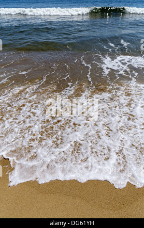 L'eau et la mousse lave-up une plage sur l'île de Plum à partir d'une déferlante Banque D'Images