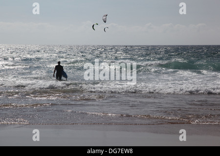 Un internaute entrant dans l'eau avec quelques kitesurfers dans l'eau à une certaine distance Banque D'Images