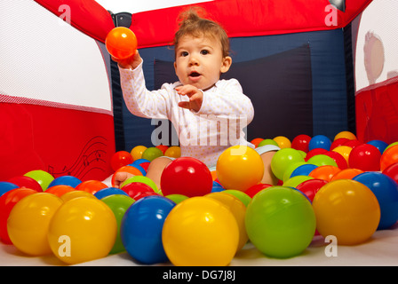 Baby Boy sitting dans un parc pour enfants avec boules colorées et lancer une balle orange Banque D'Images