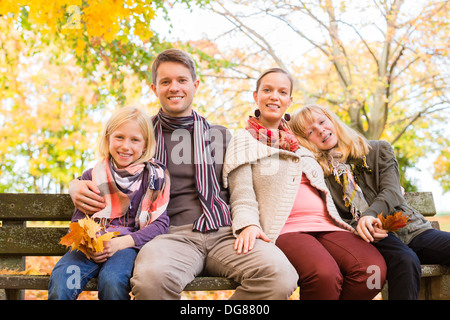 Famille heureuse, la mère, le père et les filles ou les enfants assis sur un banc en plein air avec des feuilles colorées et sous les arbres Banque D'Images