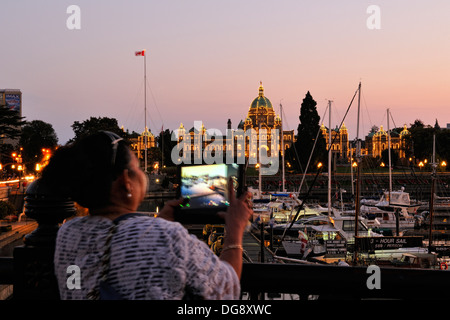 Une femme utilise son comprimé de photographier les édifices du Parlement et l'arrière-port de Victoria Victoria au crépuscule British Columbia Canada Banque D'Images