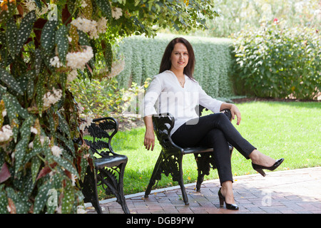 Middle aged woman sitting in cast iron chaise dans le jardin Banque D'Images