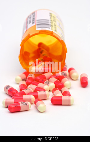 Pilules rouge et jaune répandu d'un flacon de médicaments sur un fond blanc. Banque D'Images