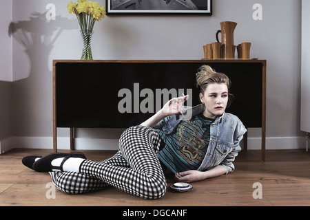 Young woman lying on floor holding cigarette Banque D'Images