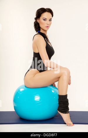 Jolie jeune femme brune en robe noire femme sportive avec blue fitness ball isolé sur fond blanc Banque D'Images