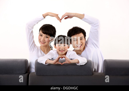 La famille de l'Asie de l'est avec un enfant assis sur le canapé, ce qui en forme de coeur Banque D'Images