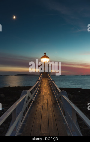 Marshall Point Lighthouse brille dans le ciel du soir sous une lune croissante sur le port à Port Port Clyde Clyde, dans le Maine. Banque D'Images