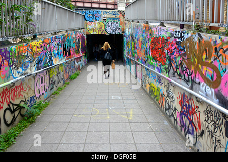 Graffiti couverts murs et vue arrière une jeune femme marchant seule vers l'inconnu dans un tunnel de métro sombre près de Waterloo station Londres Angleterre Royaume-Uni Banque D'Images