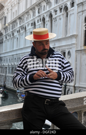 Gondolier, Venise, Vénétie, Italie. Gondolier reposant sur un pont au-dessus de l'un des canaux de Venise à la recherche à d'autres bateaux sur le canal. Banque D'Images