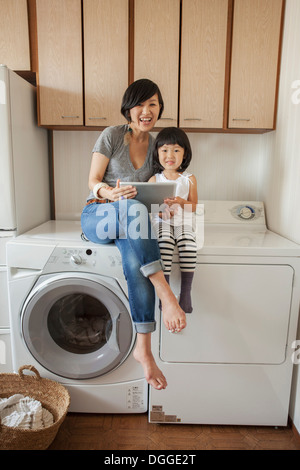 La mère et la fille assis sur un lave-linge à l'aide de tablet Banque D'Images