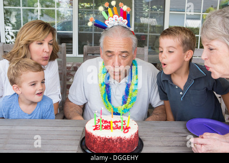 Senior man blowing out candles on cake en famille Banque D'Images